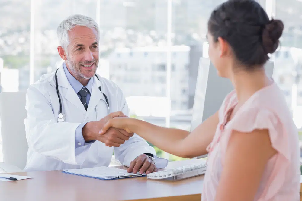 Older-male-doctor-shaking-the-hand-of-a-young-female-patient-over-desk